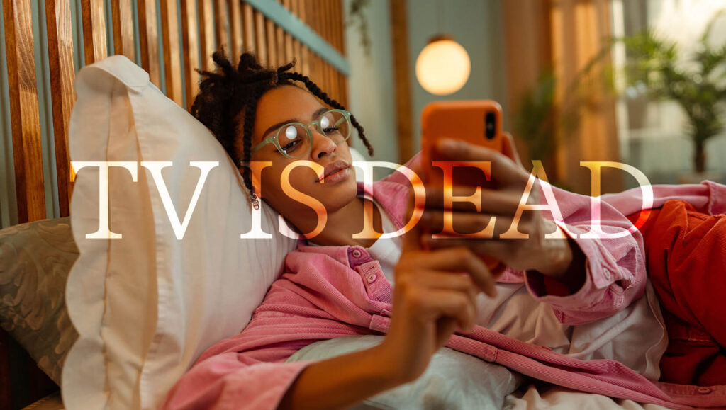 Person watching TV on a phone in bed, showing TV is dead is a myth